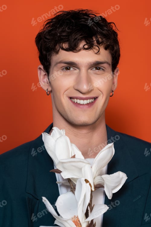 Preview: Portrait of smiling young man looking at camera near blooming magnolia isolated on red