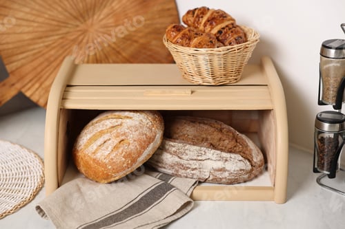 Preview: Wooden bread basket, freshly baked loaves and croissants on white marble table in kitchen