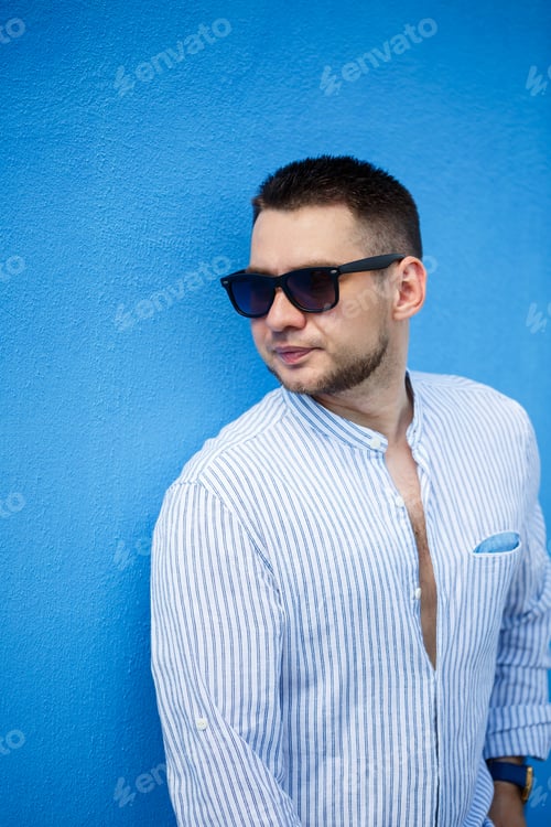 Preview: Young guy businessman in a blue shirt and black glasses on a blue background