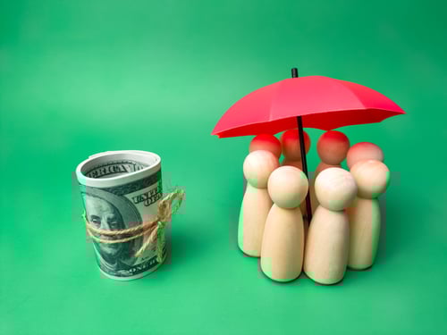 Group of wooden dolls hiding under a red umbrella with banknotes on a green background Group of wooden dolls hiding under a red umbrella with banknotes on a green background