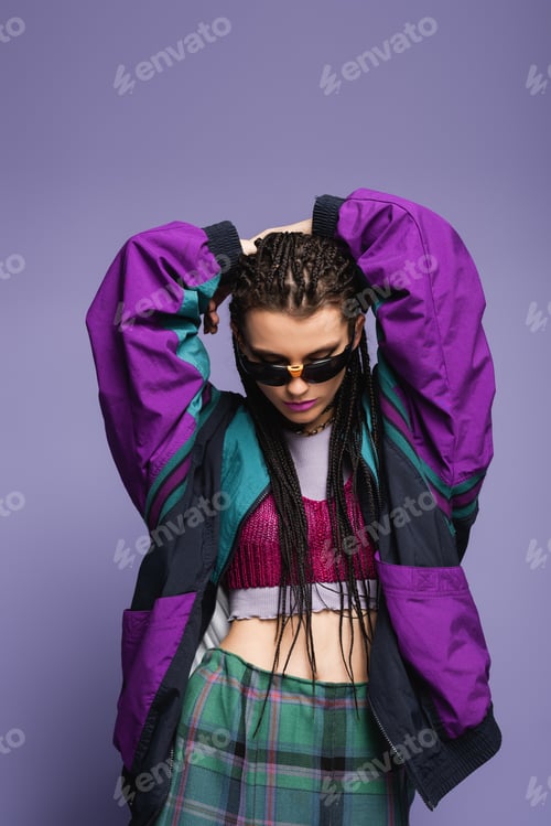 Preview: Fashionable model with braids hairstyle and retro sports jacket posing isolated on purple