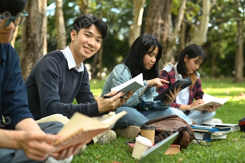 Preview: Asian student man reading books, preparing for exam on green lawn at university campus.