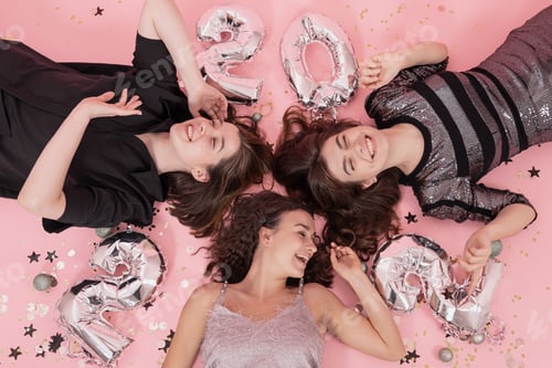 Preview: Cheerful girls lie on pink background with silver balloons 2022, top view.