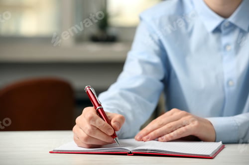 Preview: Woman writing with pen in notebook at table indoors, closeup. Space for text