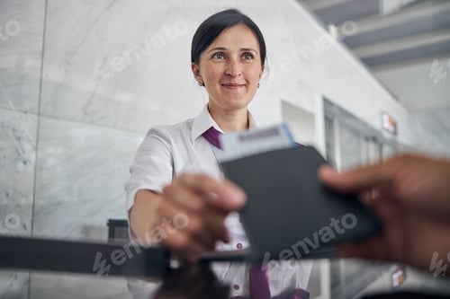 Preview: Smiling woman helping passenger with checking in at airport
