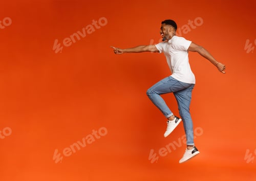 Preview: Excited african-american man jumping on orange background