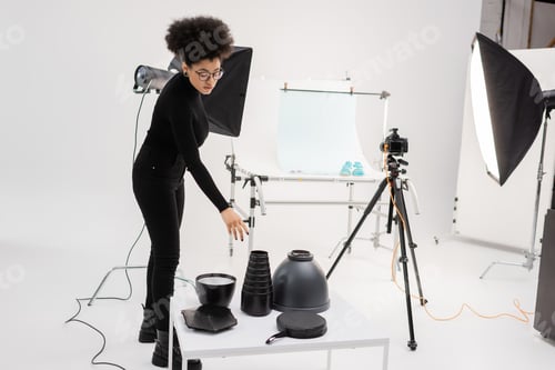 Preview: stylish african american content maker reaching lighting equipment near softbox reflector and
