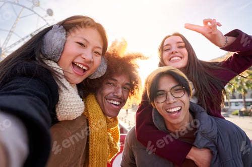 Preview: Happy selfie of group of four international friends doing piggyback outside at city at winter time.