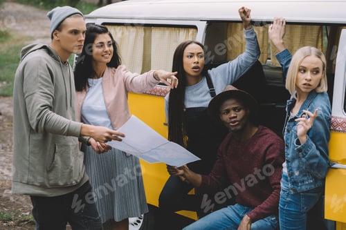Preview: young multiethnic travelers with map showing the way while standing at minivan