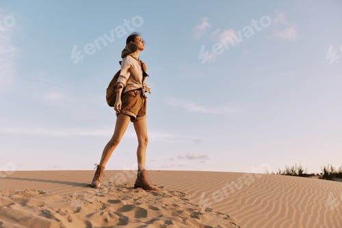 Preview: Woman walking through majestic sand dunes under a clear blue sky in a serene desert landscape