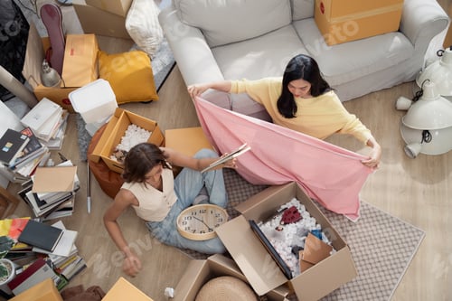 Preview: Asian girl friends unpacking stuff from cardboard boxes at the new house.