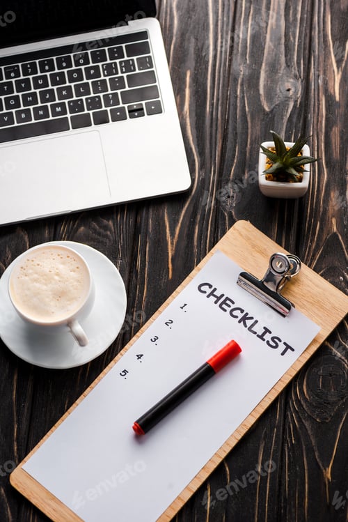 Preview: top view of laptop near clipboard with checklist, plant, red marker pen and cup of coffee on table,
