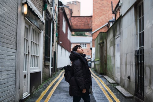 Preview: Lonely short-haired female with a black coat walking in an old neighborhood