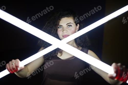 Preview: Curly brunette plus size model with two long led lamp at black room.