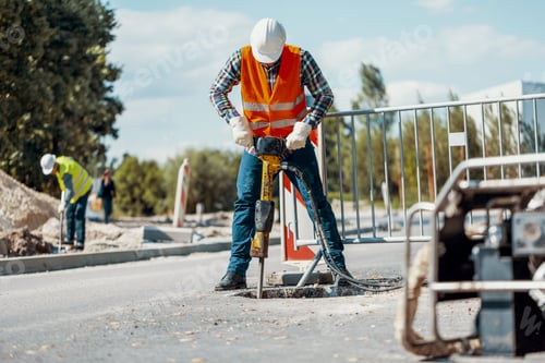 Preview: Worker in reflective vest with drill repairing street during roa