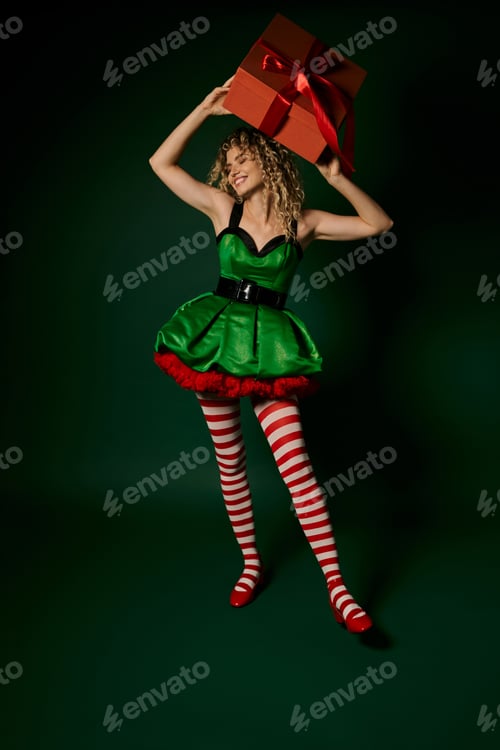 Preview: smiley new year elf in festive green dress holding present above her head and looking away