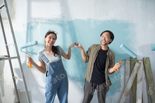 Preview: Asian couple expressing love heart while painting the wall with light blue paint using a roller