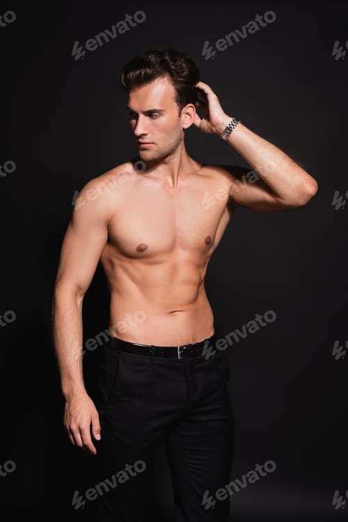 Preview: young shirtless man with muscular torso holding hand near head while posing on black