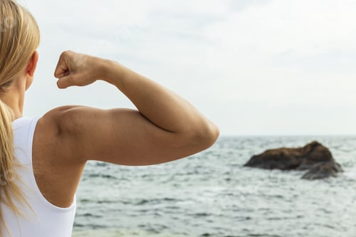 Preview: Sporty blonde girl's hand showing muscles. On the background of the sea.