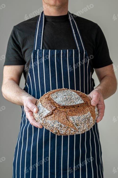 Preview: Close-up at bakers hands holding a loaf of bread in front of him.