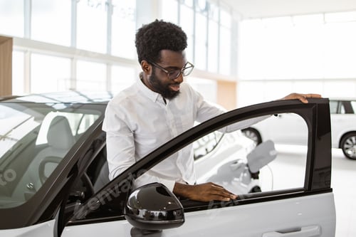 Preview: Happy man customer, client, wearing white shirt, looking at interior of car.
