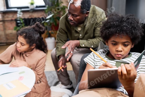 Preview: Serious intercultural schoolboy with tablet making notes in copybook