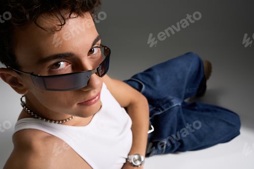 Preview: Stylish teenager with curly hair wearing sunglasses and a tank top on a grey background