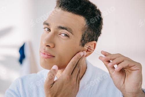 Preview: handsome man plucking temple with tweezer and looking at camera