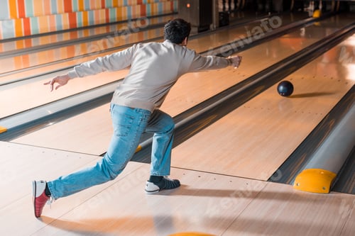 Preview: back view of young man throwing bowling ball on skittle alley