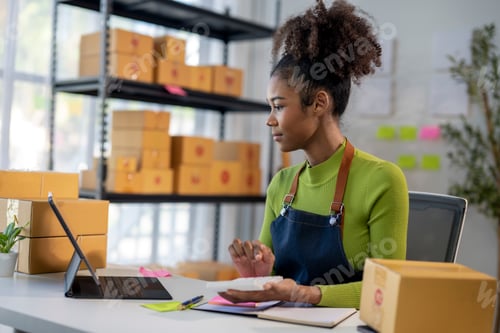 Preview: A woman is sitting at a desk with a laptop and a box of paper