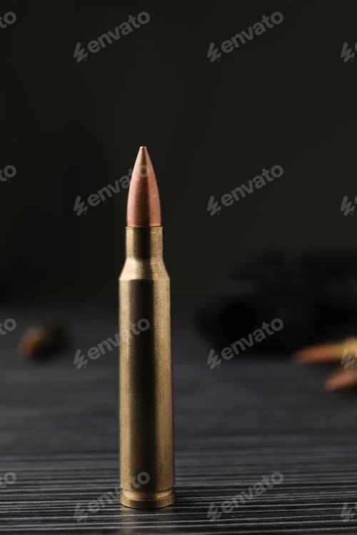 Preview: Bullet on black wooden table, closeup. Military ammunition