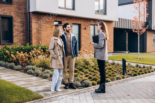 Preview: Happy couple interacting with realtor outside modern new house on the street