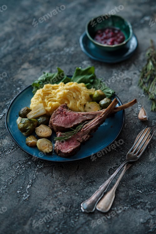 Preview: A serving of roasted rack of lamb with garnish of potatoes and greens on dark table