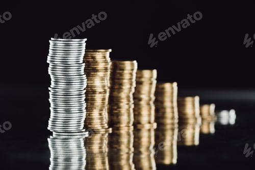 Preview: selective focus of stacked silver and golden coins on surface with reflection isolated on black