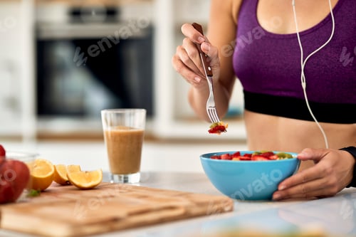 Preview: Close-up of athletic woman eating fruit salad in the kitchen.