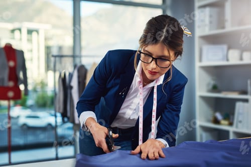 Preview: Cropped shot of an attractive young fashion designer cutting fabric in her design workshop