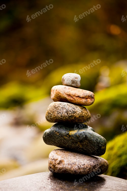 Preview: A stack of small rocks balanced on top of each other by a river.