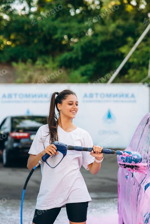 Preview: Woman with high pressure hose stands by car covered in pink foam
