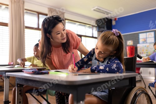 Preview: Diverse female teacher and schoolgirl in wheelchair in elementary school class