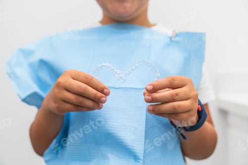 Preview: Boy holding a clear dental aligner before dental checkup with orthodontist.