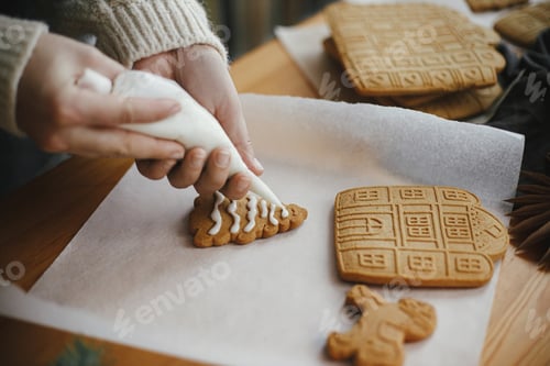 Preview: Hands decorating christmas gingerbread cookies with icing on wooden table with candle and ornaments