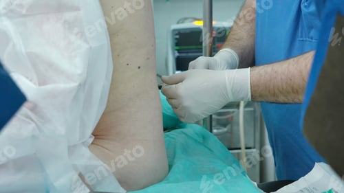 Preview: Surgeon prepares patient for surgery. Creative. Patient sits with back to surgeon during operation