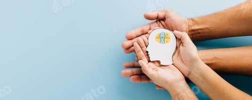 Preview: Hands holding a brain jigsaw in a head paper cut symbolize Down Syndrome awareness.
