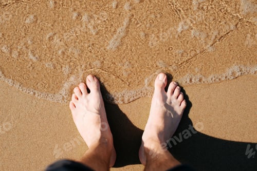 Preview: Top view bare caucasian male feet on seashore on sunny summer day, close-up
