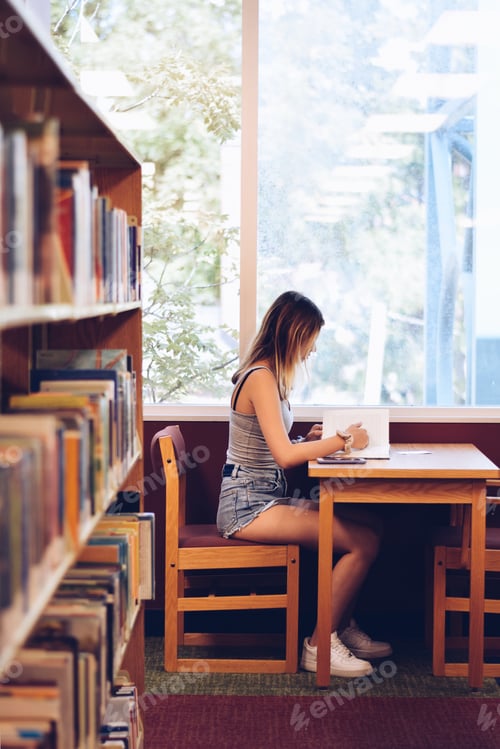 Preview: Young teenage girl sitting at a table in the library and reading a book
