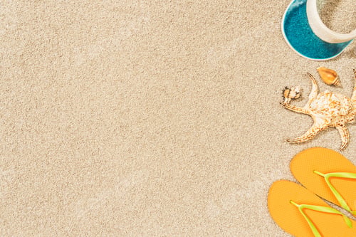 Preview: flat lay with arrangement of seashells, yellow flip flops and blue cap on sand