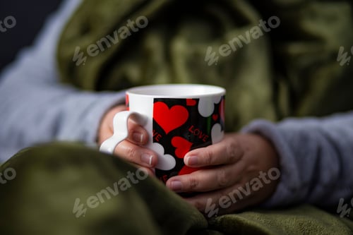 Preview: Adult woman holding a cup of hot drink with a blanket on her body