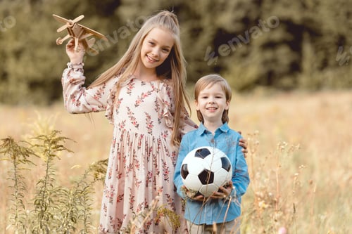 Preview: adorable little kids with toy airplane and football ball standing together in field
