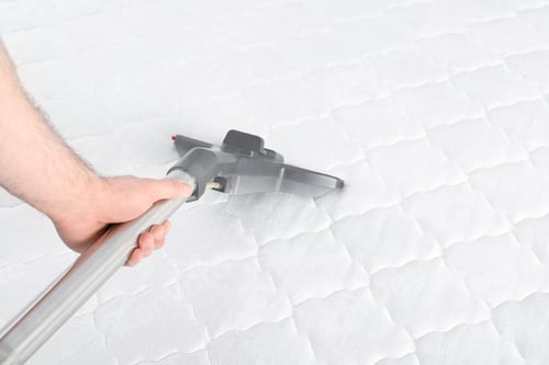 Preview: Man disinfecting mattress with vacuum cleaner, closeup. Space for text