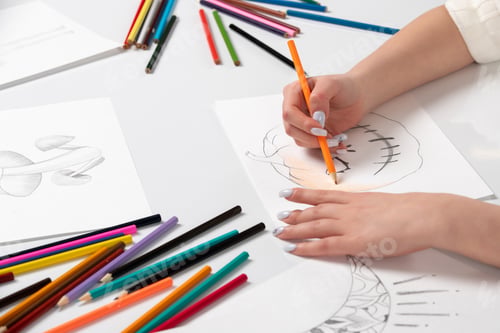 Preview: Drawing a young girl hand drawing a halloween pumpkin with orange pencil behind the table